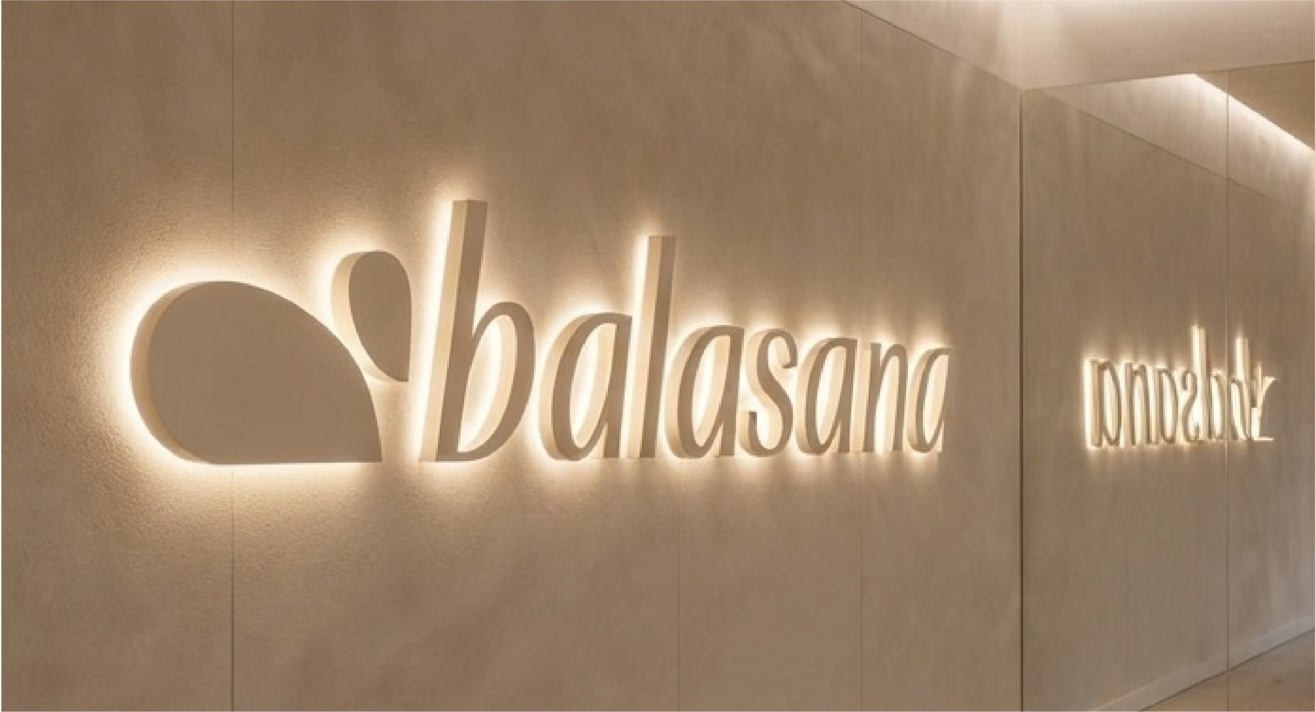 Backlit “bhavans” logo and emblem on a warm beige interior wall with a reflected sign on the right.